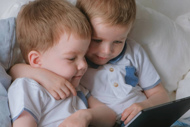 Kids with tablet. Two boys twins toddlers looking cartoon at tablet lying on the bed. - Foto, Bild