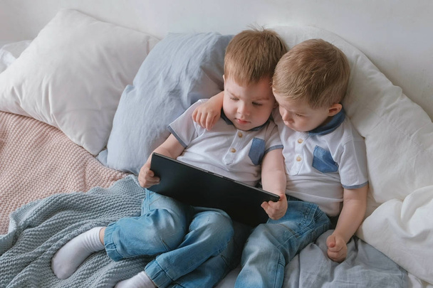 Kids with tablet. Two boys twins toddlers looking cartoon at tablet lying on the bed. - Фото, зображення