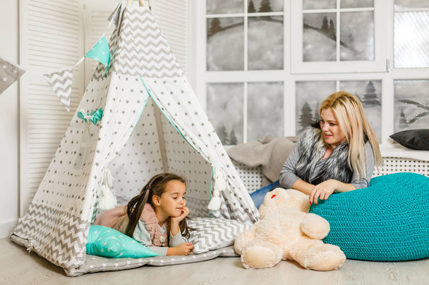 Jonge blonde moeder tijd doorbrengen met dochter in stijlvolle slaapkamer - Foto, afbeelding