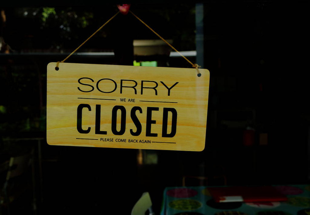 hölzernes geschlossenes Schild, das am Schaufenster eines Geschäfts hängt, mit den Worten "Entschuldigung, dass wir geschlossen sind, bitte kommen Sie wieder zurück" - Foto, Bild