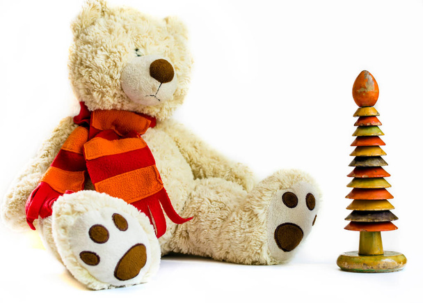 Χνουδωτό αρκουδάκι με κόκκινο μαντήλι και ξύλινη δαχτυλίδι στοίβαξης σε άσπρο φόντο. Παλιά vintage παιχνίδια. - Φωτογραφία, εικόνα