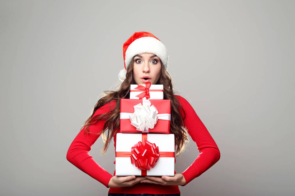 Young woman in santa hat with gift boxes on grey background - 写真・画像