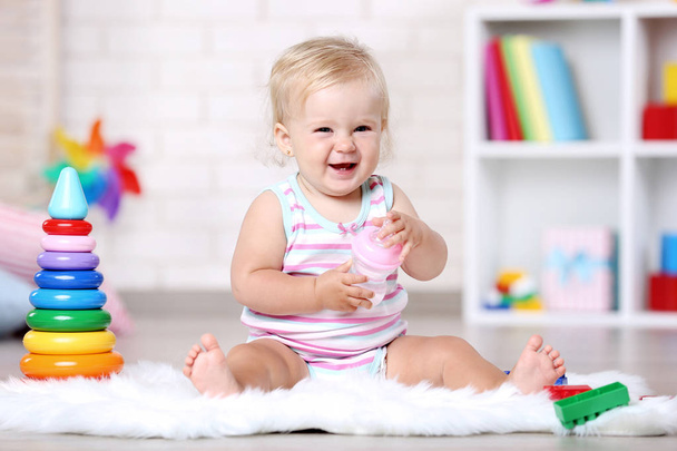 Baby girl with bottle sitting on white carpet - 写真・画像