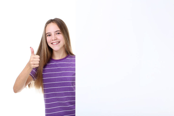 Young girl standing near blank board and showing thumb up on white background - 写真・画像