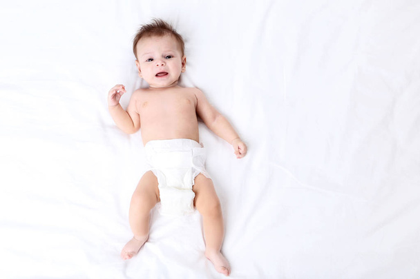 Cute baby in diaper lying on white bed - Valokuva, kuva