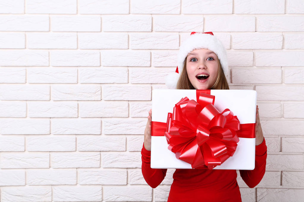 Young girl holding gift box on brick wall background - Foto, Imagem