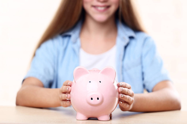 Young girl with pink piggybank sitting at table - Photo, Image