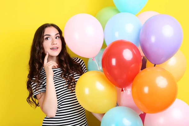 Cute girl with colored balloons on yellow background - Фото, зображення