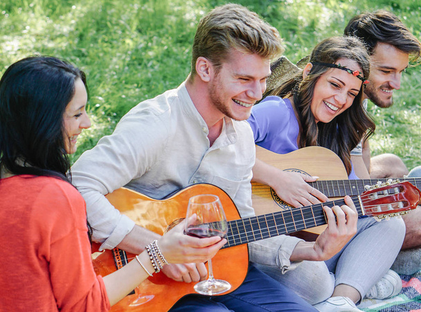 Grupa znajomych gry gitara i śmiejąc się podczas picia czerwonego wina siedzi na trawie w parku odkryty - szczęśliwy młodych ludzi zabawy razem Dokonywanie koncepcji życia młodzieży piknik - przyjaźń, - Zdjęcie, obraz