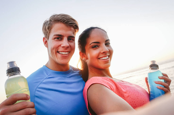Couple sportif prenant un selfie avec téléphone portable au coucher du soleil - les jeunes ayant une pause de l'entraînement et boire des boissons énergisantes - Sport, relation, mode de vie sain concept
 - Photo, image