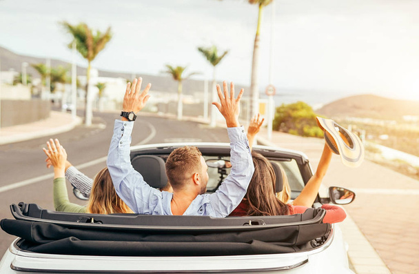Amis heureux de s'amuser en voiture convertible au coucher du soleil en vacances - Les jeunes faisant la fête et la danse dans une voiture de cabrio pendant leur voyage sur la route - Amitié, Voyage, concept de style de vie des jeunes
 - Photo, image