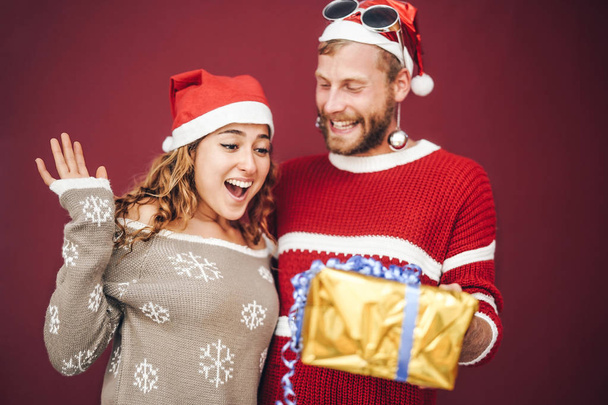 Happy boyfriend surprising his girlfriend giving her a christmas present - Young couple having fun celebrating xmas holidays - Love, millennial relationship concept - Фото, изображение