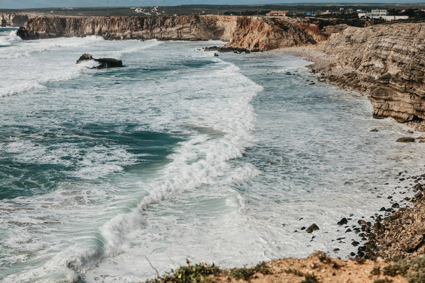 Vista dall'alto delle onde e bella acqua blu con schiuma bianca dell'Oceano Atlantico sulla riva rocciosa al largo della costa del Portogallo
. - Foto, immagini
