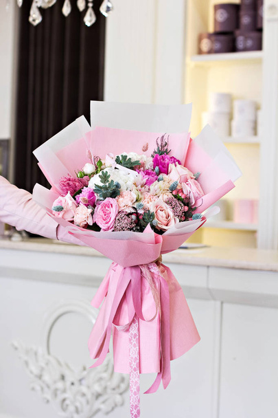 Beautiful bouquet wiht rose and and ranunculus flower in pink wrapping paper in female hands. Roses and other delicate beautiful flowers. - Фото, изображение