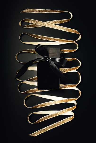 black perfume bottle with bow and shiny golden ribbon on black - Fotoğraf, Görsel
