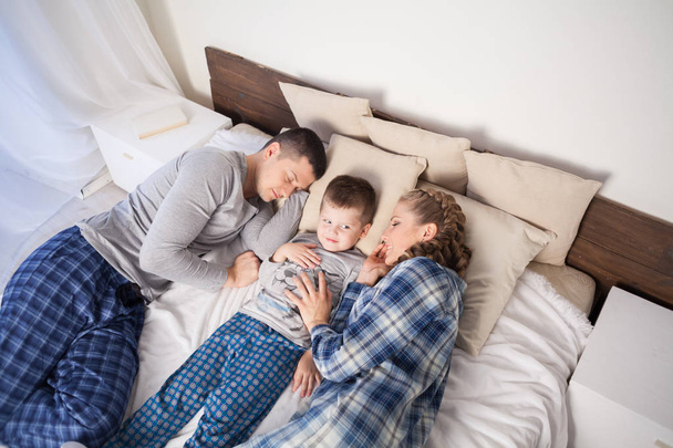 μαμά, μπαμπάς και γιος το πρωί ξαπλωμένη στο κρεβάτι στο σπίτι - Φωτογραφία, εικόνα