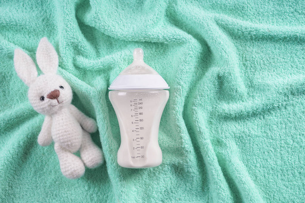 Biberón de leche para bebé con juguete para conejito en una toalla suave, vista superior
 - Foto, Imagen