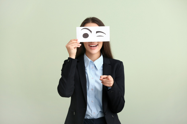 Mujer joven y emocional escondiendo la cara detrás de una hoja de papel con los ojos dibujados sobre un fondo claro
 - Foto, Imagen