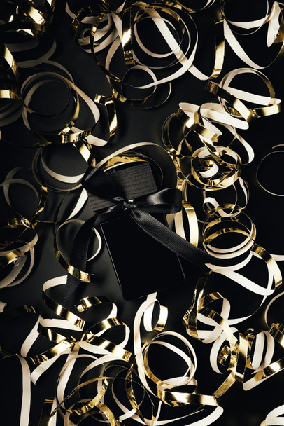 top view of black perfume bottle with golden ribbons on black - Foto, Imagen