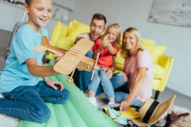 boy playing with toy wooden airplane with family having fun on background and packing for summer holiday - Photo, Image