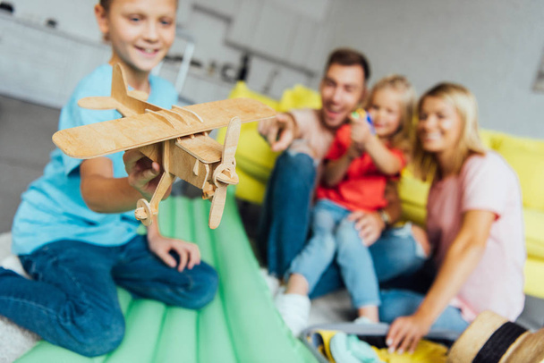 menino brincando com brinquedo avião de madeira com a família se divertindo no fundo
 - Foto, Imagem