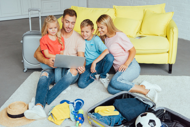 glückliche Familie mit Laptop, Planung des Sommerurlaubs, Koffer packen und Spaß haben, Reisekonzept - Foto, Bild