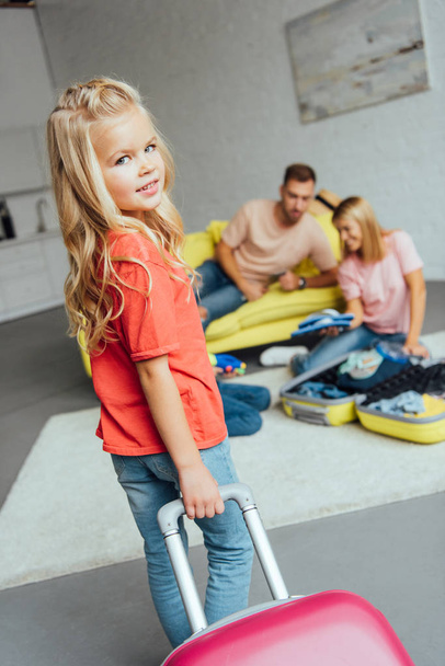 kid holding suitcase while family packing for summer vacation on background, travel concept - Photo, Image