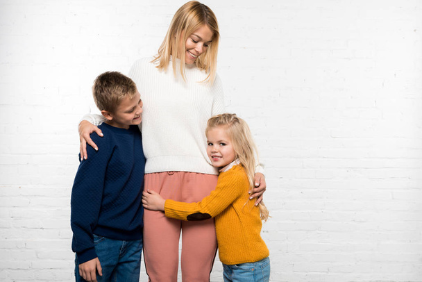 glückliche Mutter umarmt Sohn und Tochter auf weißem Hintergrund - Foto, Bild