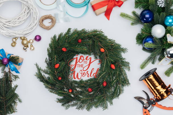 το Top view χειροποίητο στεφάνι διακοσμήσεων Χριστουγέννων, ψαλίδι και κορδέλες που απομονώνονται σε λευκό με έμπνευση «χαρά στον κόσμο» - Φωτογραφία, εικόνα