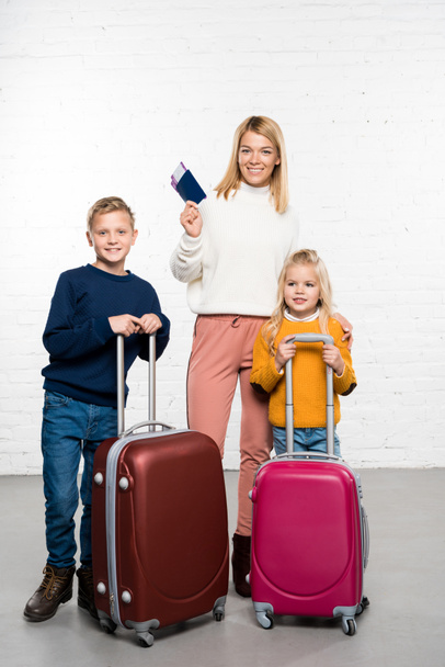 Happy mother holding passport and tickets while children holding suitcases ready to go on winter trip, on white background - Photo, Image