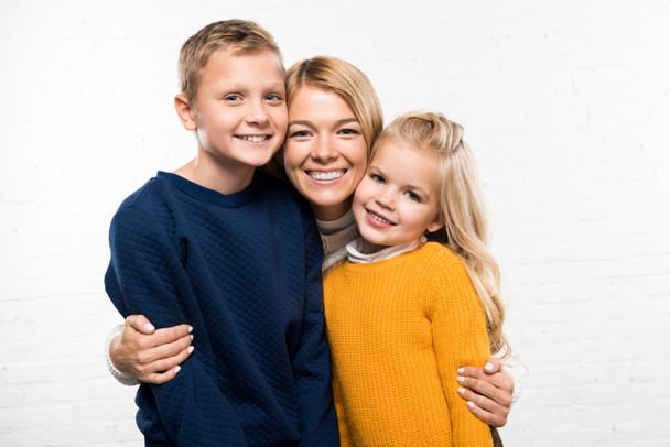 happy mother hugging son and daughter looking at camera on white background - Photo, Image