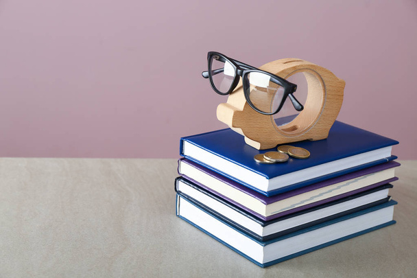 Piggy bank, a szemüveg és a verem a könyvek tábla. A megtakarítások az oktatási koncepció - Fotó, kép