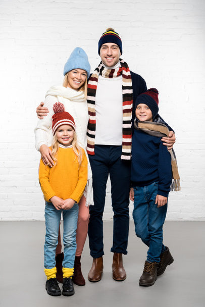 happy family in winter clothes hugging and looking at camera on white background - 写真・画像