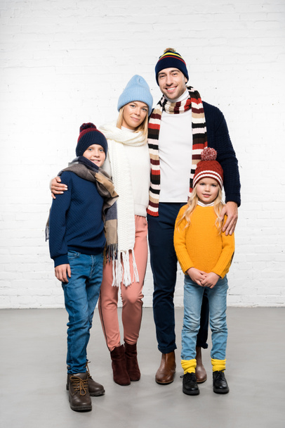 smiling family in winter clothes hugging and looking at camera on white background - 写真・画像