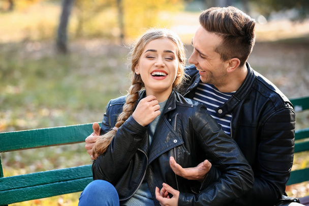 Αγαπώντας το νεαρό ζευγάρι κάθεται σε ξύλινο παγκάκι στο πάρκο φθινόπωρο - Φωτογραφία, εικόνα