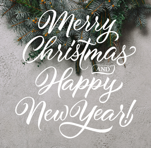cropped image of fir wreath for Christmas decoration hanging on grey wall with "merry christmas and happy new year" lettering - 写真・画像