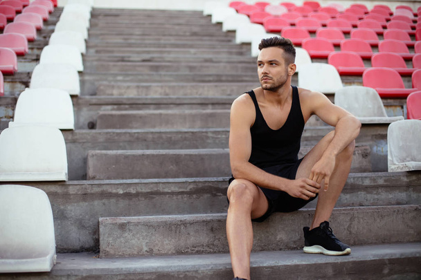 Handsome man relaxing on stadium stairs after workout. rest and sport concept  - Foto, afbeelding