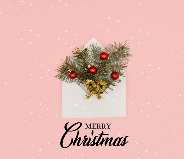 felülnézete a fenyő gallyak, csillogó karácsonyi baubles elszigetelt rózsaszín "boldog karácsonyt" betűkkel és a hó fehér boríték - Fotó, kép