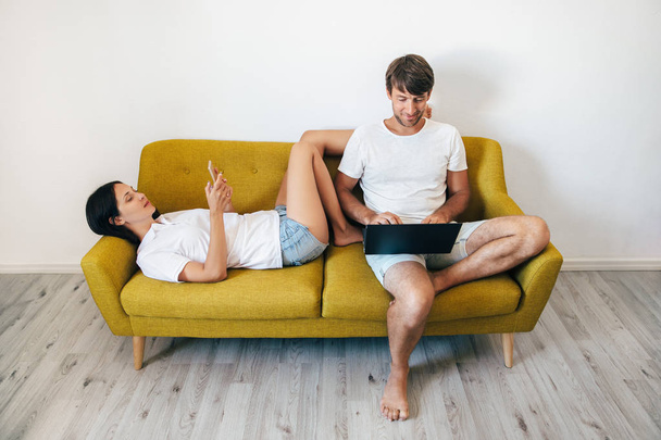 Young couple using gadgets while relaxing together at home - Zdjęcie, obraz
