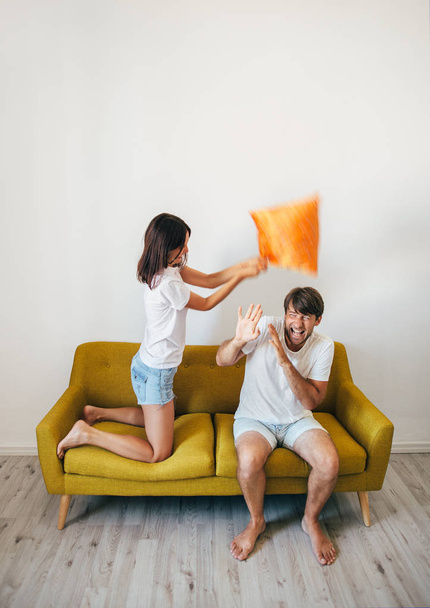 Happy young couple having fun. Woman beating scared boyfriend with pillow on bed. Fighting with pillows. fooling around concept - Fotó, kép