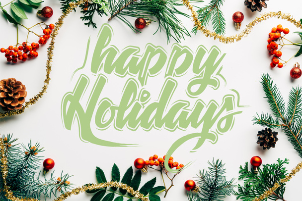 flat lay with festive arrangement of pine tree branches, common sea buckthorn and christmas decorations on white tabletop with "happy holidays" lettering - Photo, Image