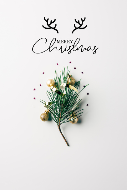 top view of little pine tree branch with ribbon and christmas balls on white surface with "merry christmas" lettering with deer horns - Fotó, kép