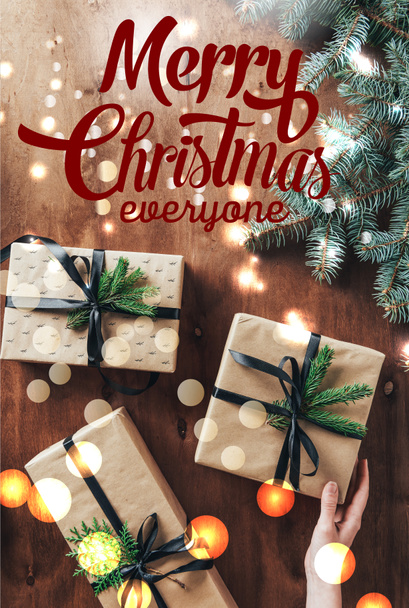 vista recortada de la mujer tocando cajas de regalo sobre fondo de madera con ramas de árbol de Navidad y letras de "Feliz Navidad a todos"
  - Foto, Imagen