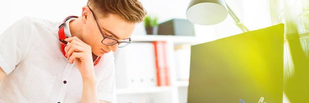 A young man in glasses stands near a computer desk. A young man draws a marker on a magnetic board. On the neck, the guys headphones hang. - 写真・画像
