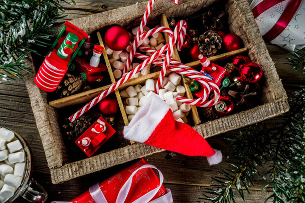 klassischer Weihnachtshintergrund, Christbaumschmuck und -zweige, Kinderspielzeug zum neuen Jahr, Zuckerstangen, Tannenzapfen, Weihnachtsmützen und Geschenkboxen auf alten hölzernen Tischplatten - Foto, Bild
