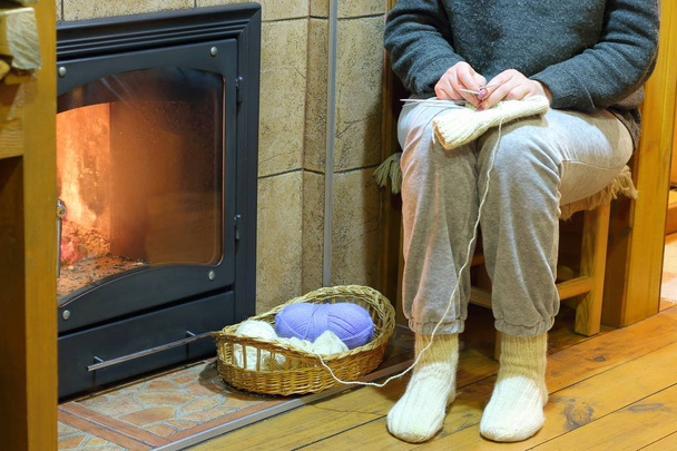 暖炉の横にある靴下を編む女性. - 写真・画像