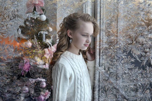 girl in a white sweater at the window at christmas - Photo, Image