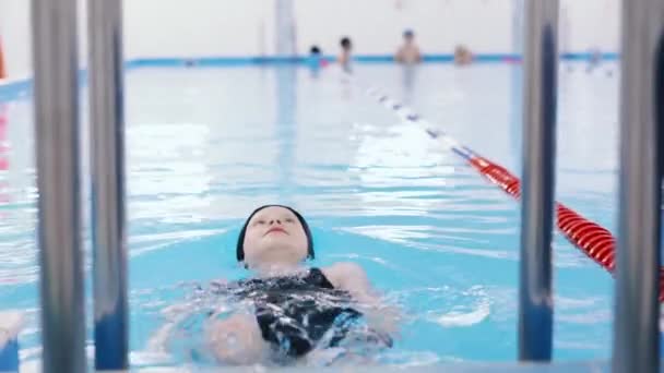 μαθήματα κολύμβησης για παιδιά στην πισίνα - όμορφη κοπέλα με ανοιχτόχρωμο δέρμα που κολυμπά στο νερό - Πλάνα, βίντεο