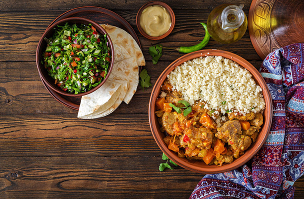 Traditional tajine dishes, couscous and fresh salad on rustic wooden table. Tagine lamb meat and pumpkin - Photo, Image
