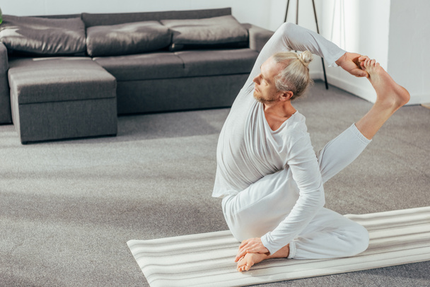 Hochwinkel-Ansicht des athletischen flexiblen erwachsenen Mannes, der zu Hause Yoga praktiziert - Foto, Bild